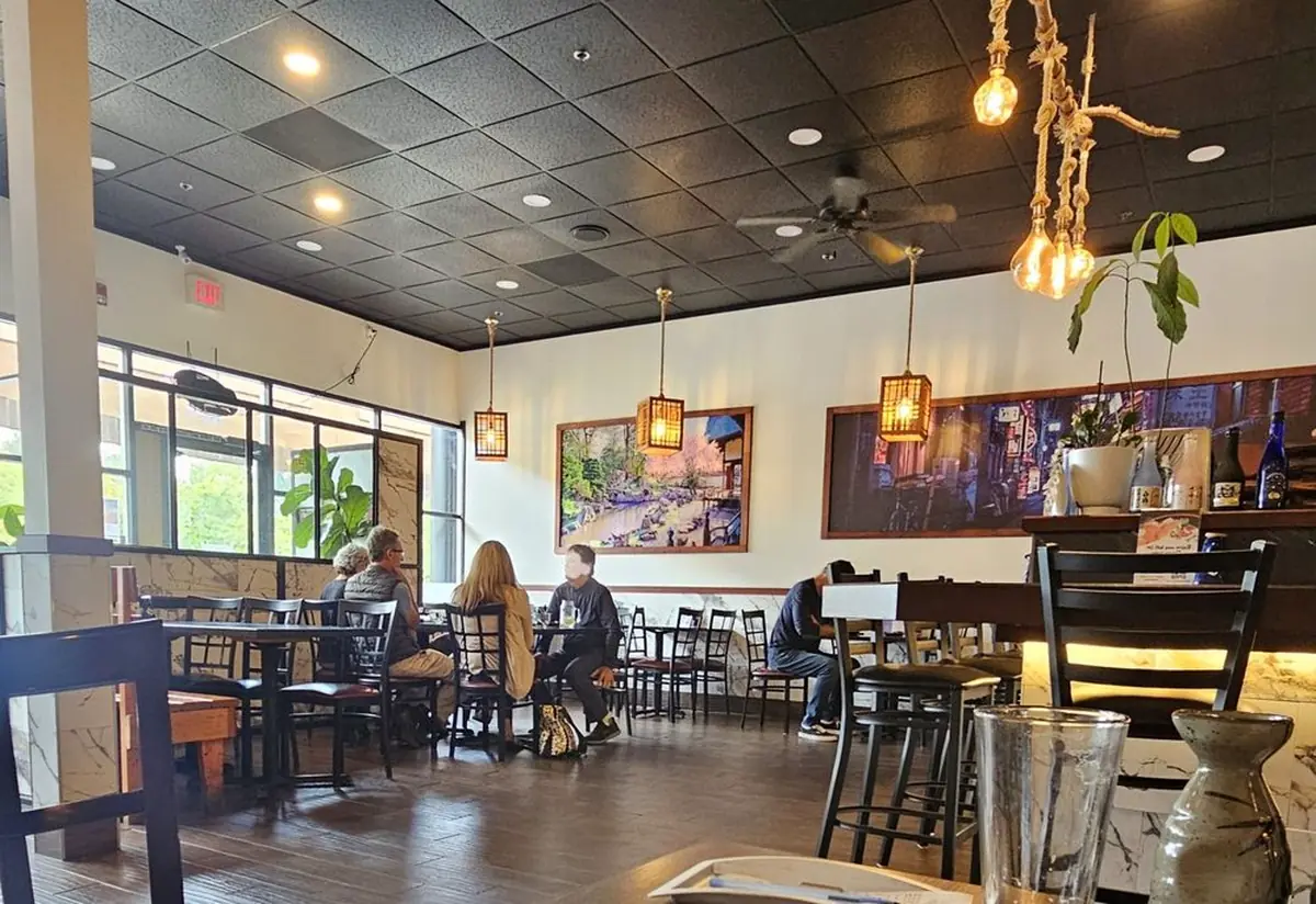 The dining room at Toro Sushi: white walls, wood floors, pendant lights and guests at tables
